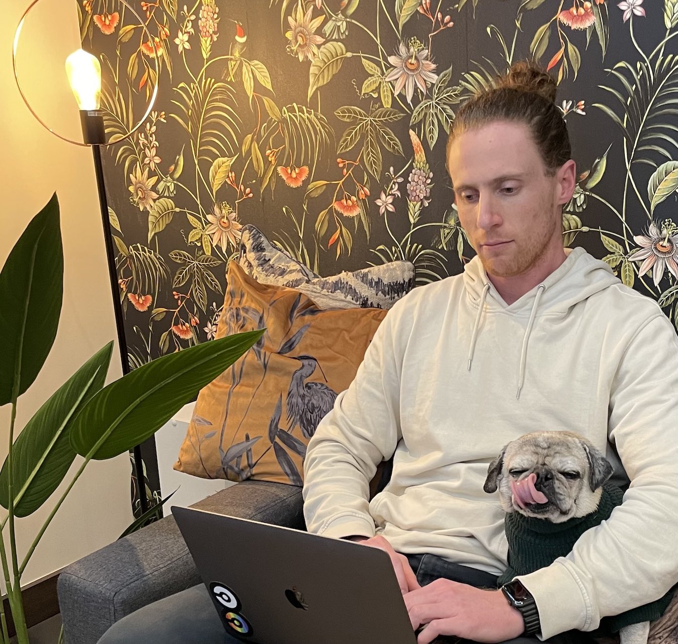 A team member sitting on a couch working on a laptop with their dog in between their arms.