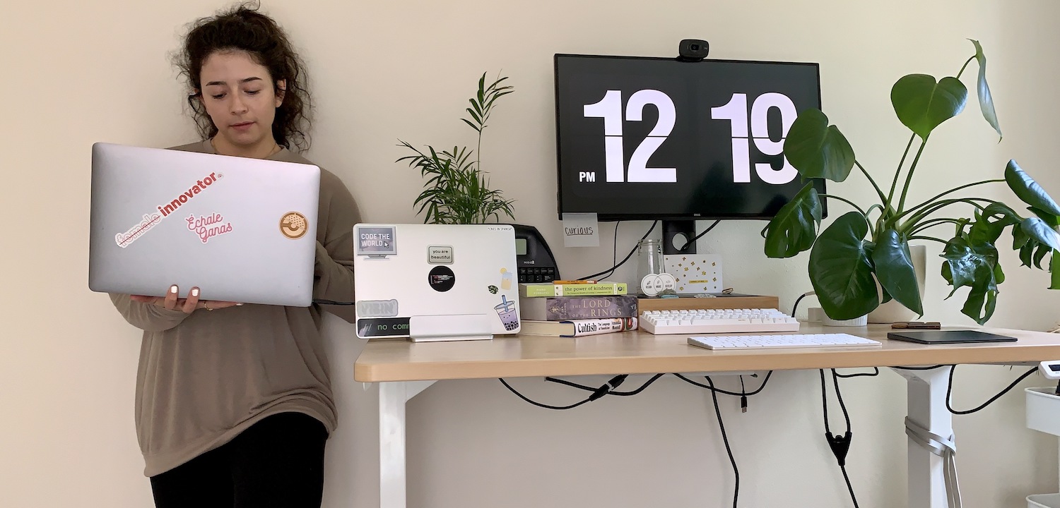 A team member beside their stand up desk with a large monitor that tells the time.